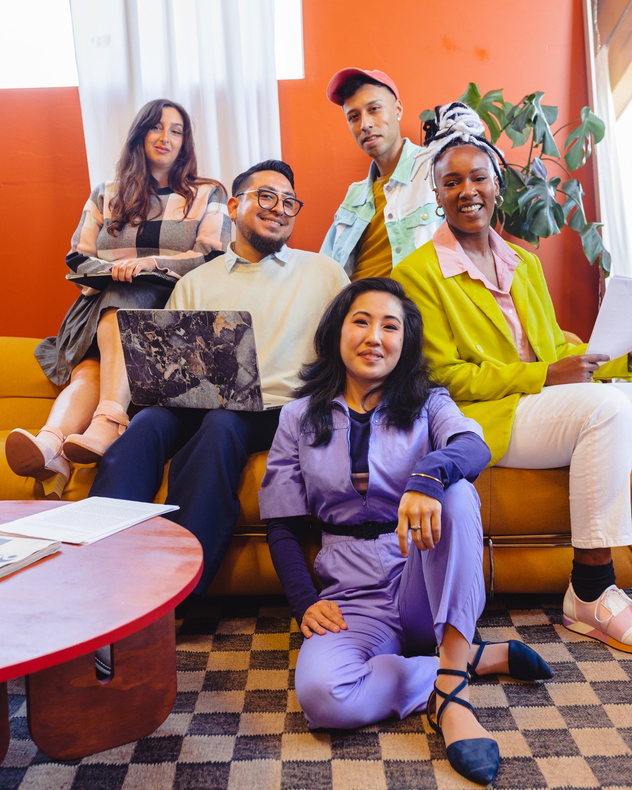 a photo of a group of people sitting on a and around a couch, smiling at the camera